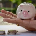 Close-up of a pink piggy bank in hand, with coins on a table, symbolizing financial savings and management.
