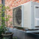 Air conditioning unit on a brick wall, with a potted plant nearby, representing Jerry Brittingham A/C & Heat, Inc. services.